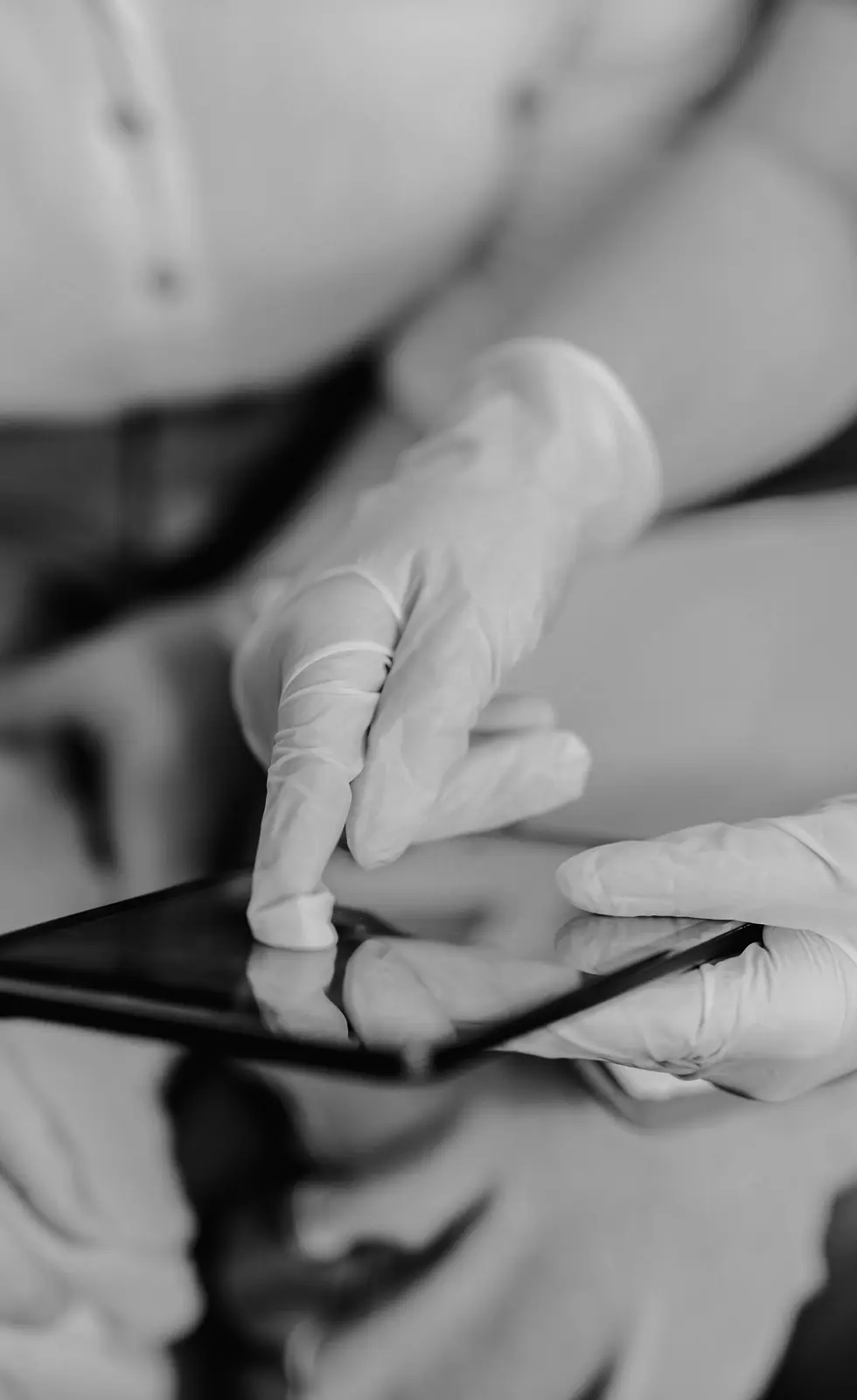Gloved hands operating a tablet in a clinical setting