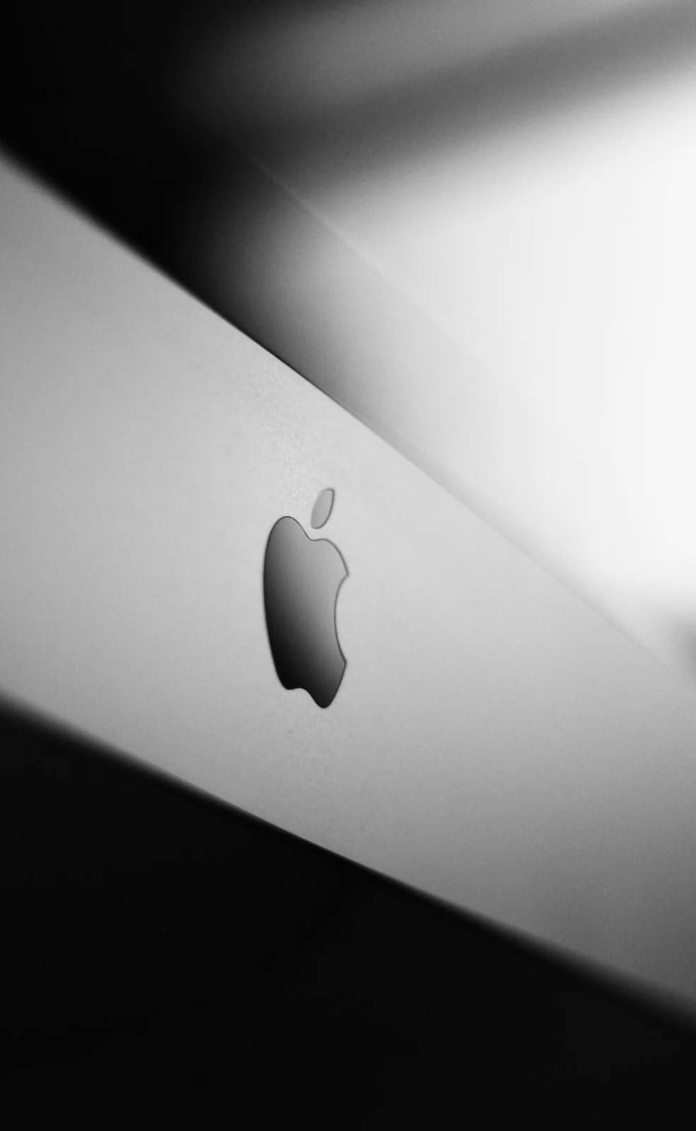 Apple logo on a silver lid, caught in a diagonal band of light