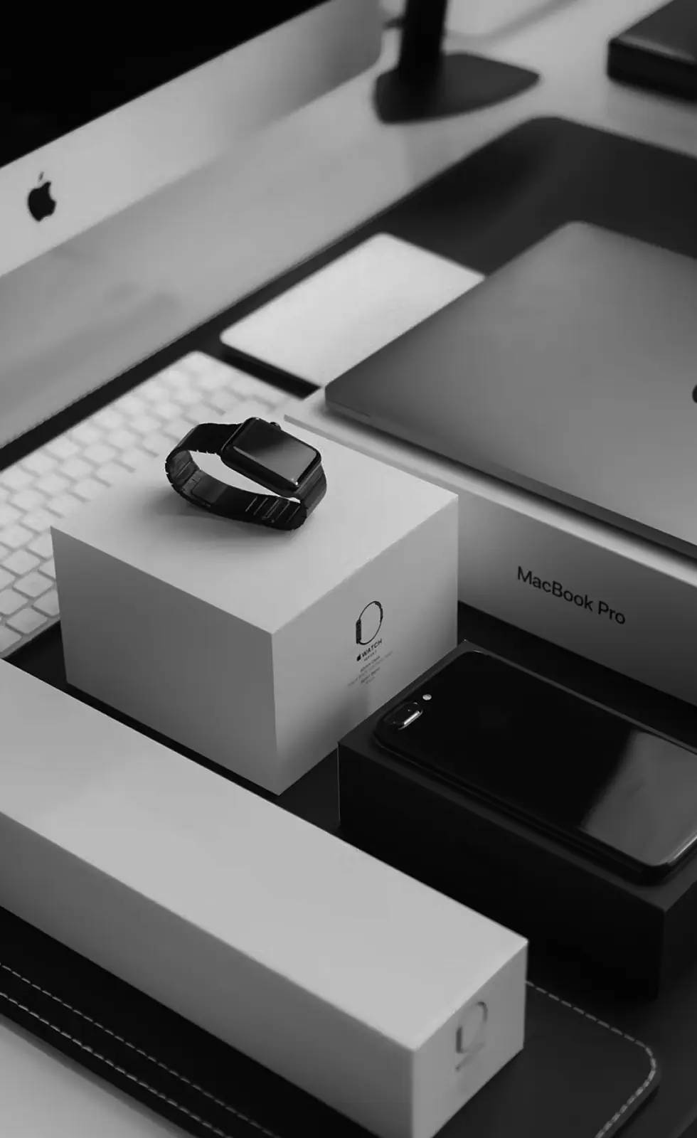Apple Watch and iPhone on a desk beside a MacBook Pro and iMac